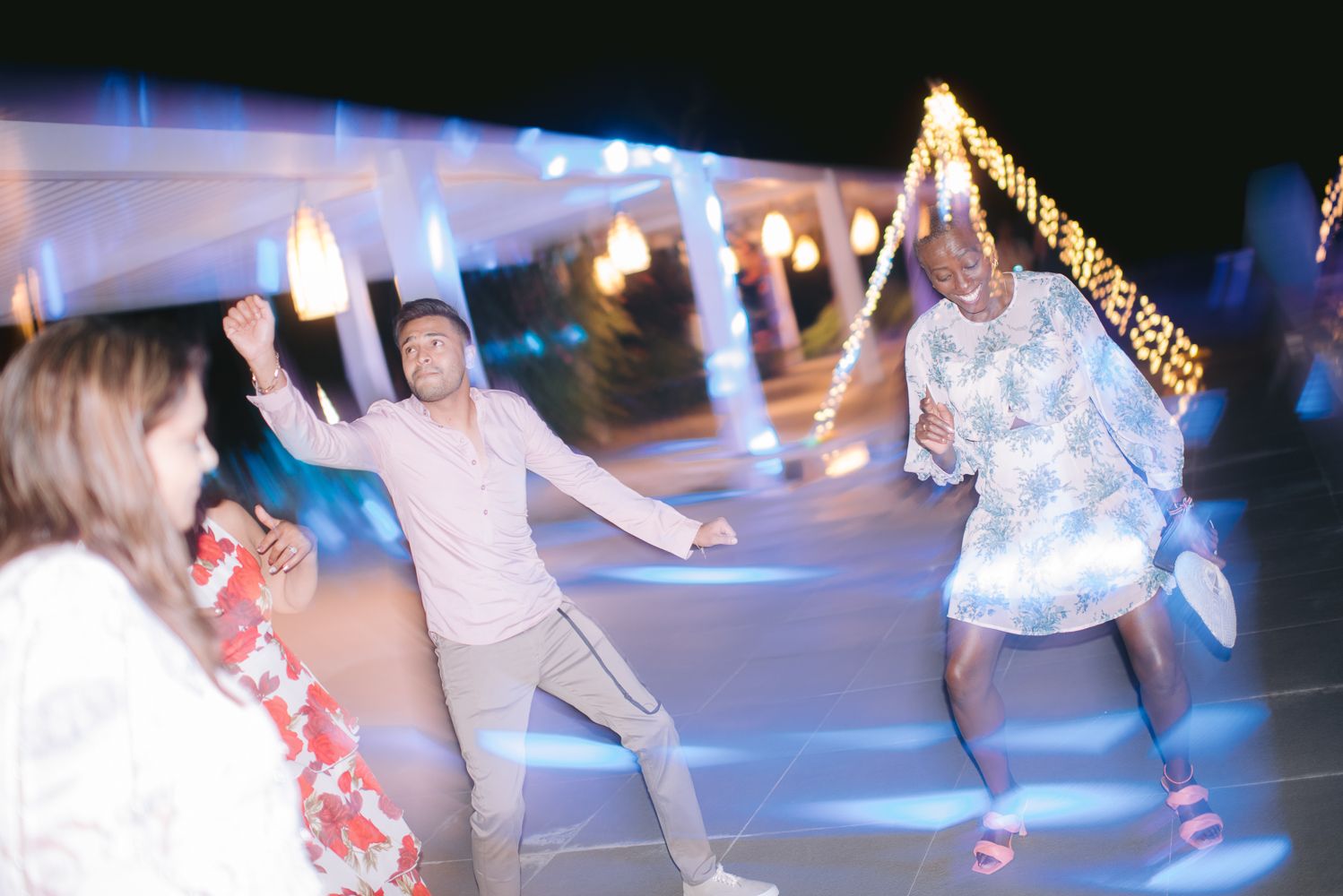 Two people dancing joyfully at an outdoor evening event with blue lights and decorative string lights in background.