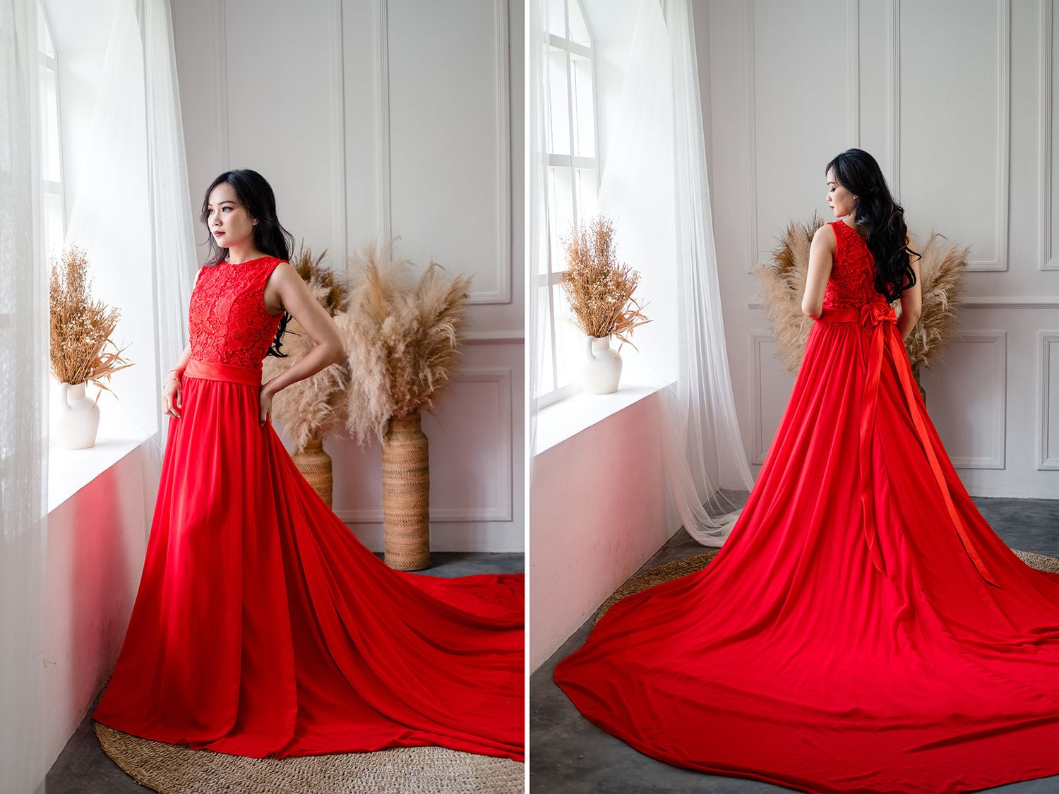 Woman in elegant red gown with lace bodice and flowing train poses by a bright window in a studio.