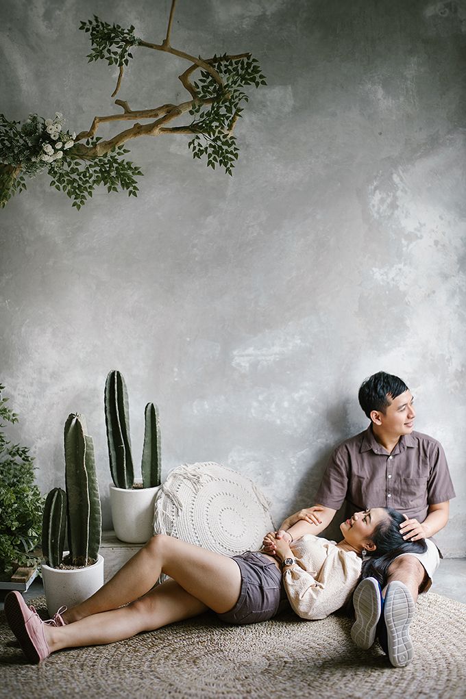 Couple relaxing together on a woven rug beside cacti and plants against a gray textured wall.