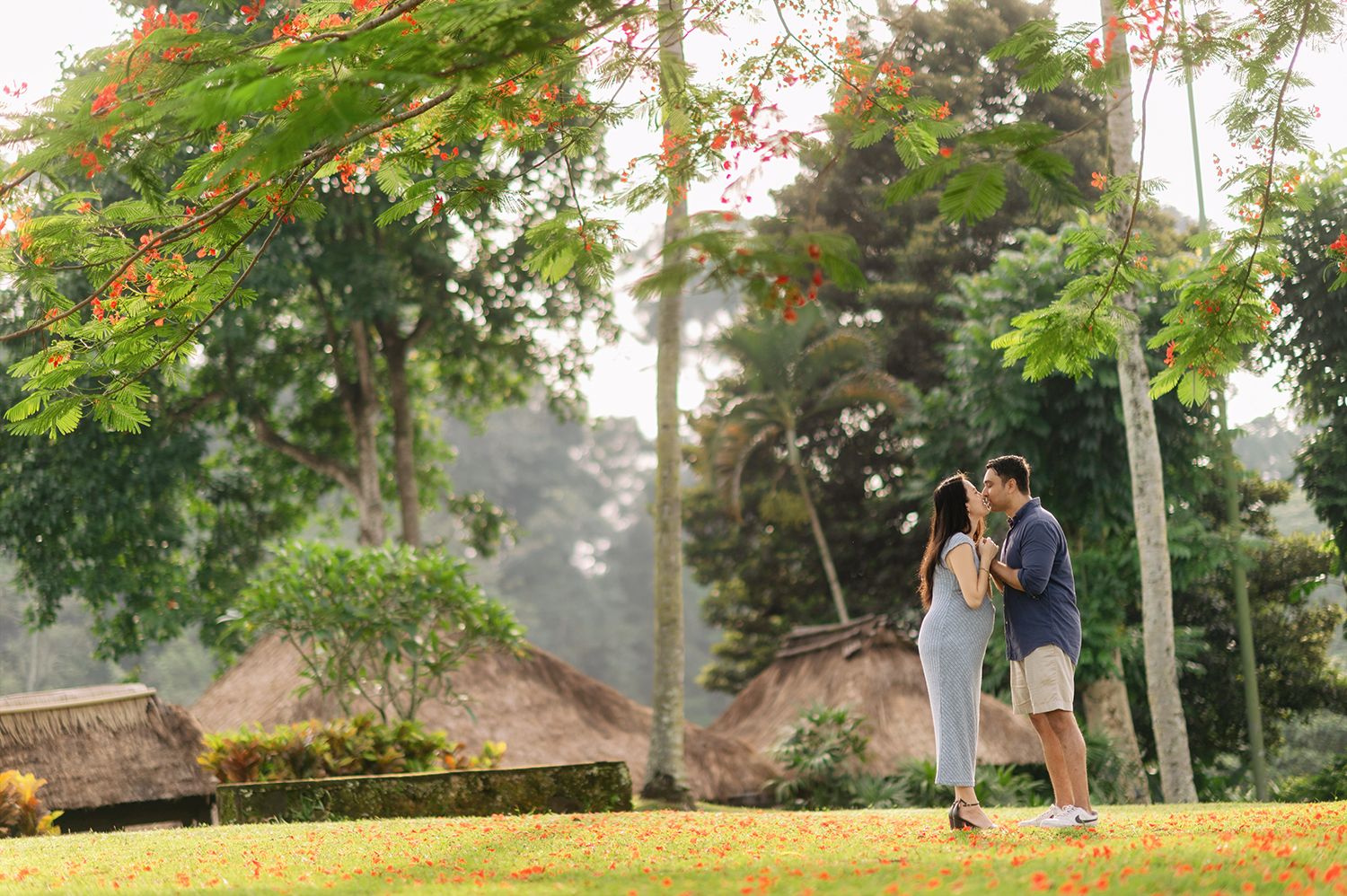 Couple sharing a romantic moment under a vibrant red flowering tree in a lush tropical garden setting Maya Ubud Resort and Spa in Bali.