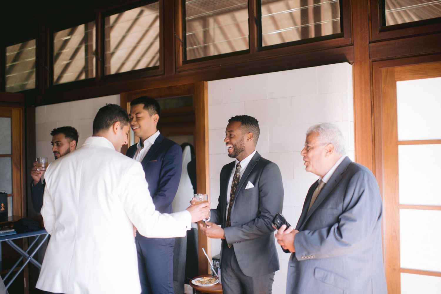 Men in suits shaking hands and conversing at a wedding reception in an elegant wood-paneled venue.