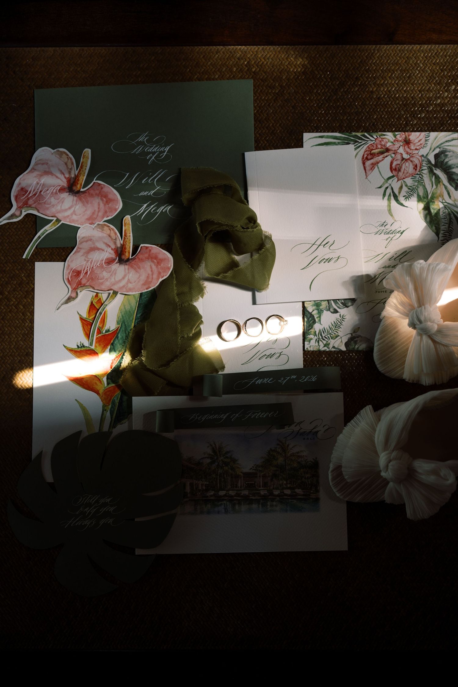 Elegant wedding stationery flat lay with floral illustrations, calligraphy invitations, and rings on a dark background.