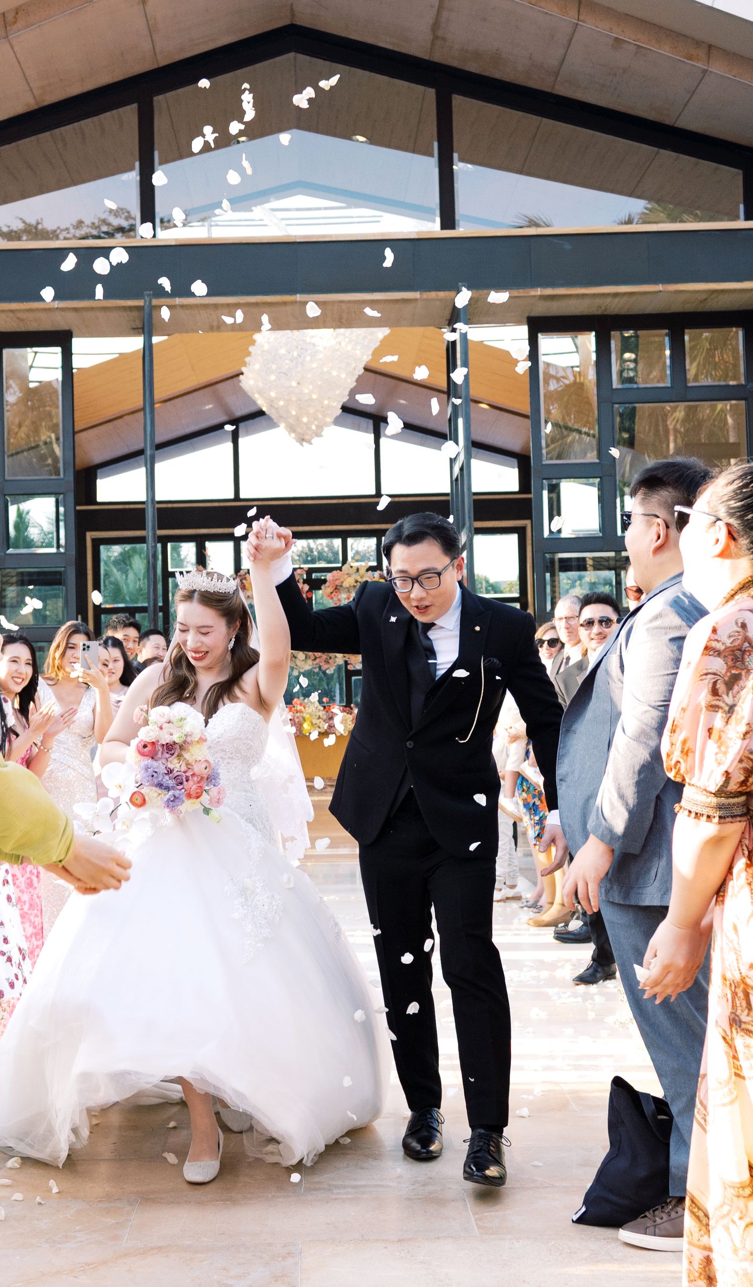 A joyful bride and groom exit their wedding ceremony as guests toss white flower petals in celebration.