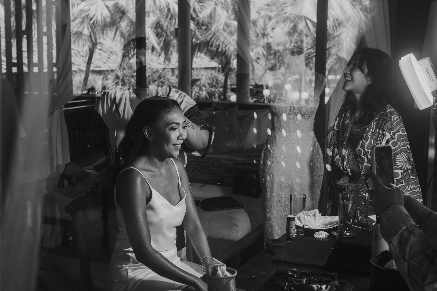 Black and white photo of a bride getting ready with a makeup artist in a tropical venue.