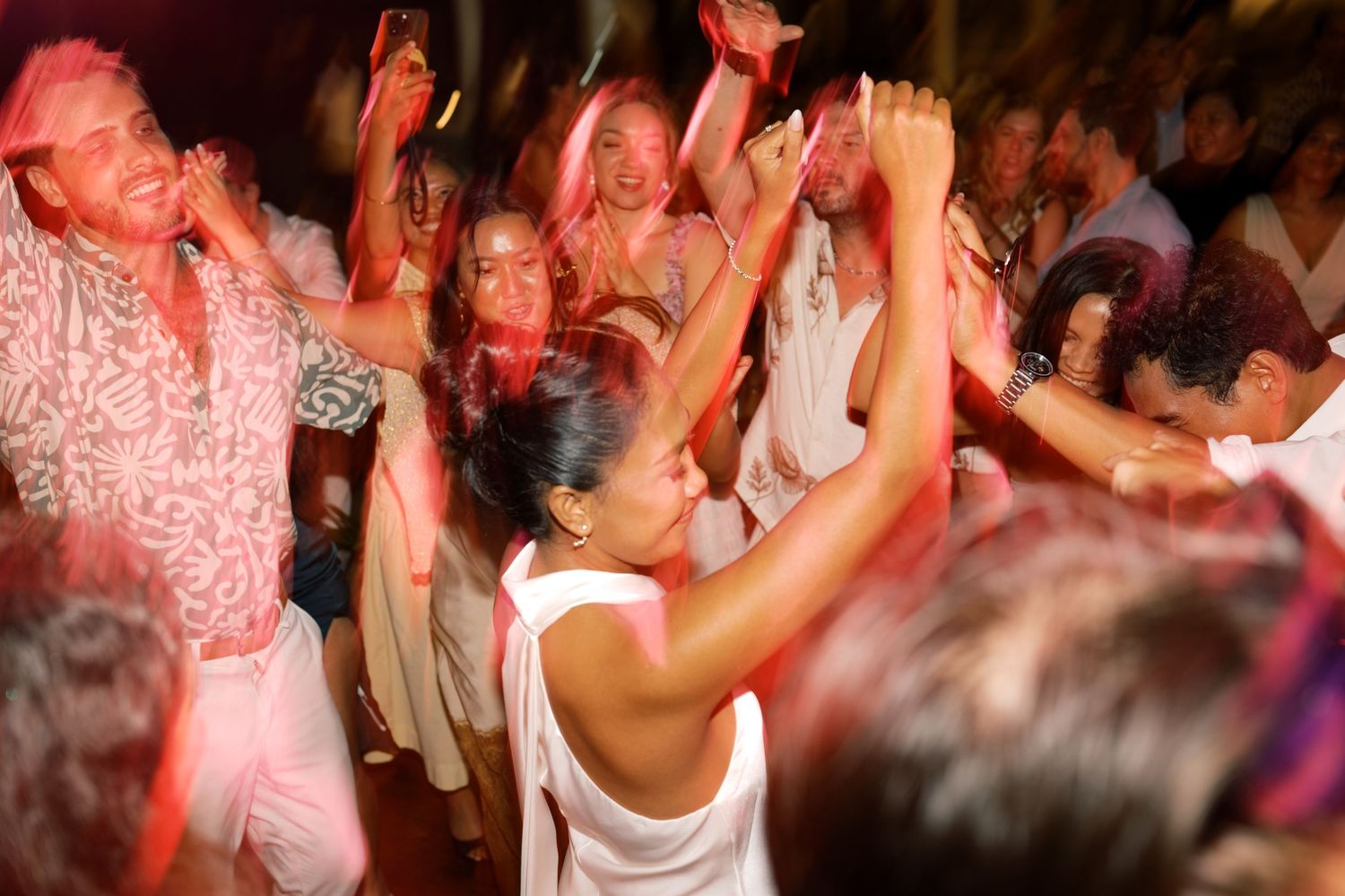 Wedding guests dancing energetically under pink lights at a lively tropical wedding reception.