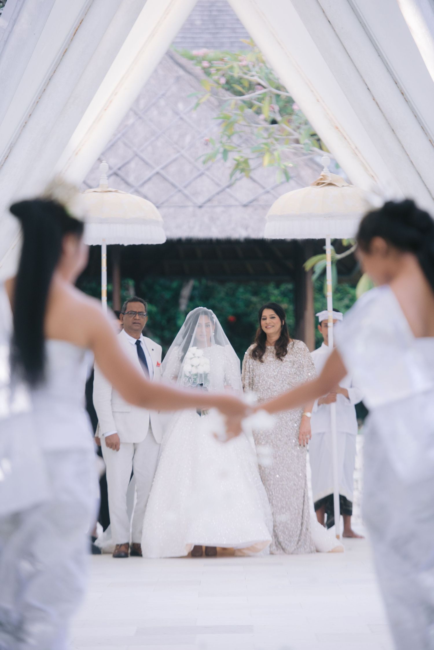 Elegant outdoor wedding ceremony with bride in white gown and veil, officiant, and bridesmaids under a draped canopy.