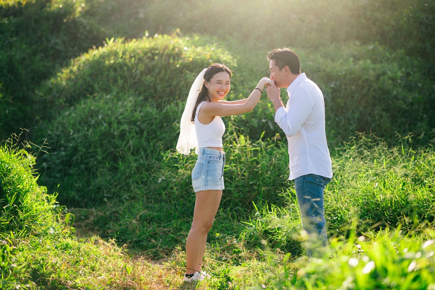 A couple dances together in a sunlit green meadow, the woman wearing a white top and denim shorts.