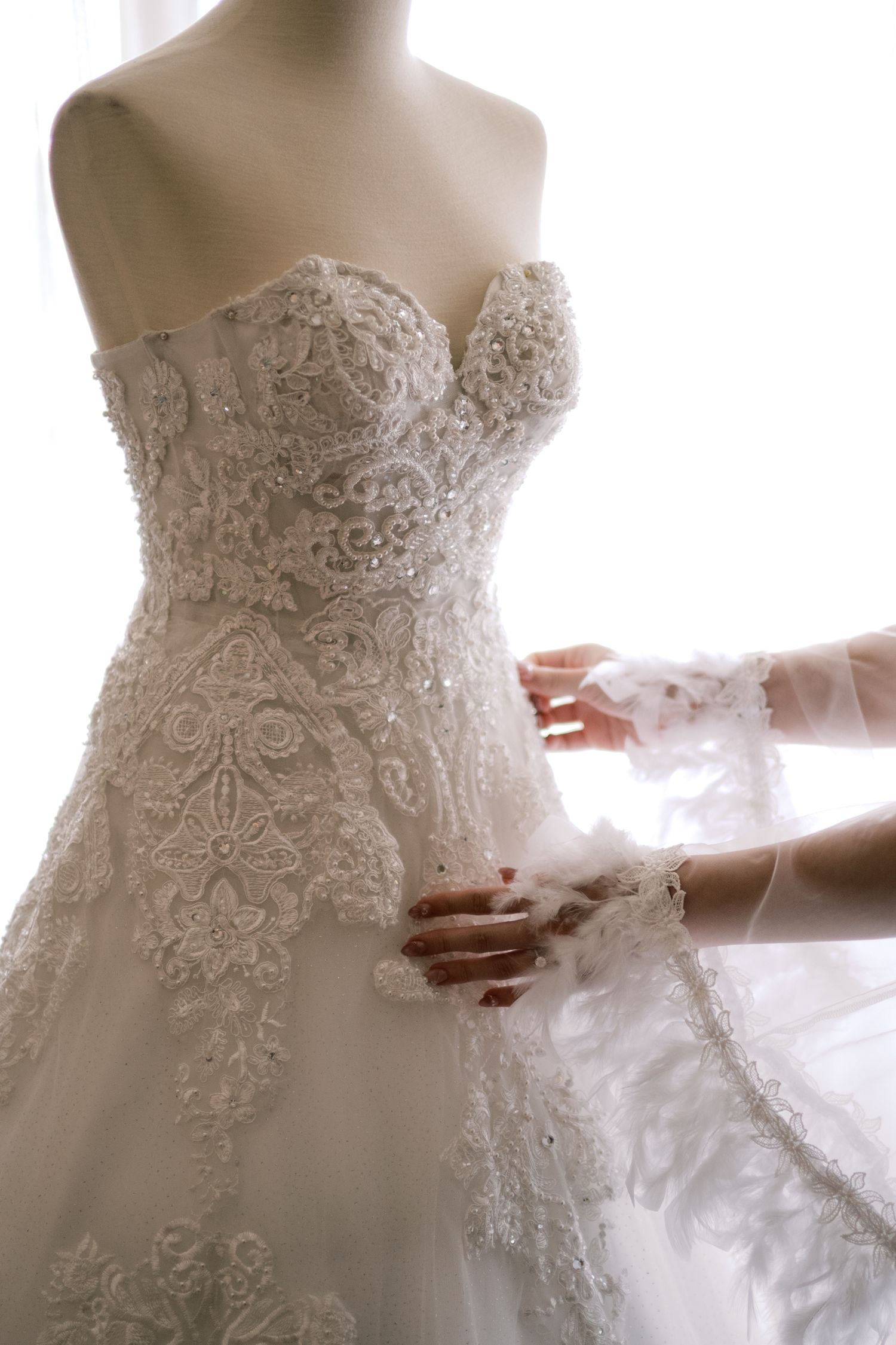 Elegant strapless wedding gown with intricate lace embroidery and beading displayed on a mannequin being fitted.