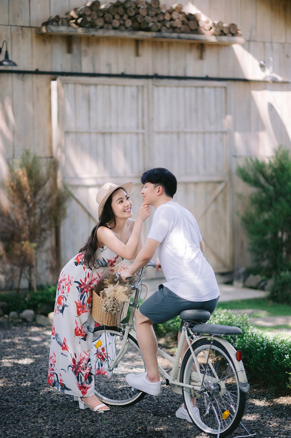 A smiling couple shares a romantic moment beside a vintage bicycle with a flower basket near a rustic barn.