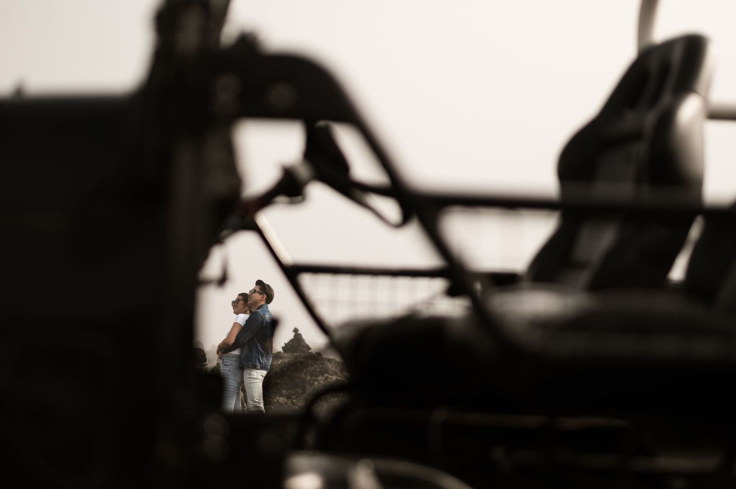 A golfer swings a club on a course, framed between heavy machinery in the foreground.