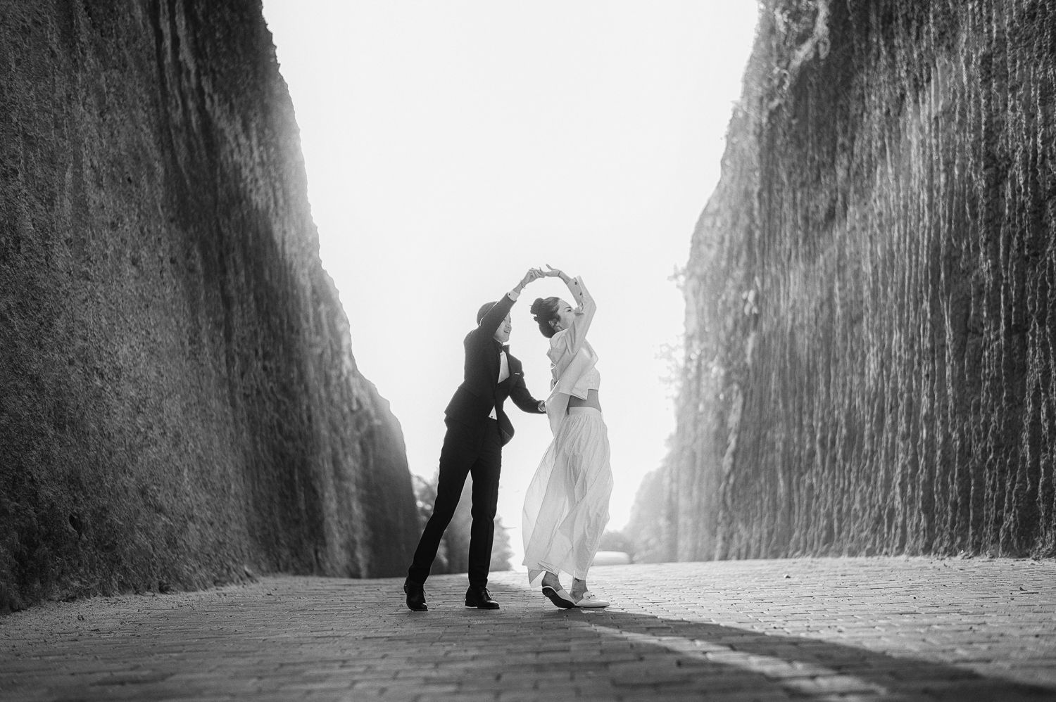 Two people dancing between towering rock walls in a dramatic black and white photograph.