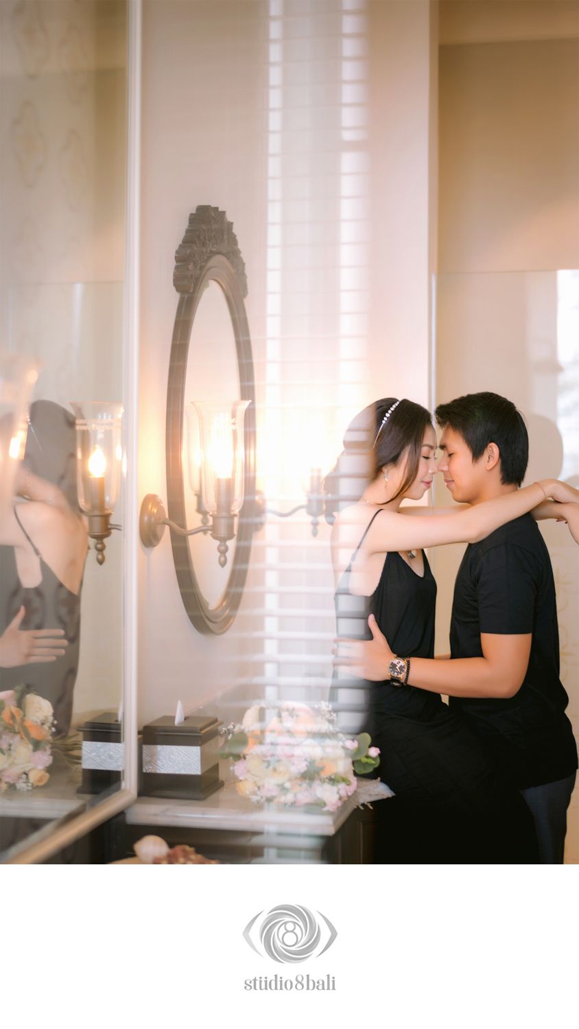 Romantic couple in black outfits embracing near a vintage mirror with candlelight, captured by Studio 8 Bali.