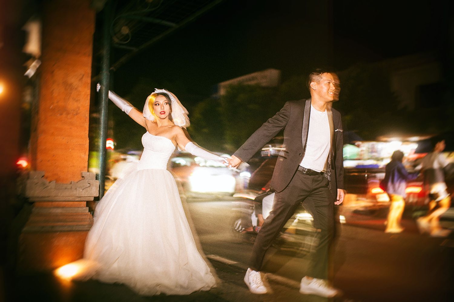 Bride and groom crossing a busy city street at night, with motion blur capturing their joyful energy.