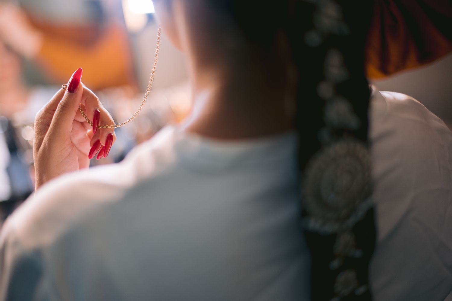Bride with braided hair and red nails holding a delicate necklace during wedding preparations.