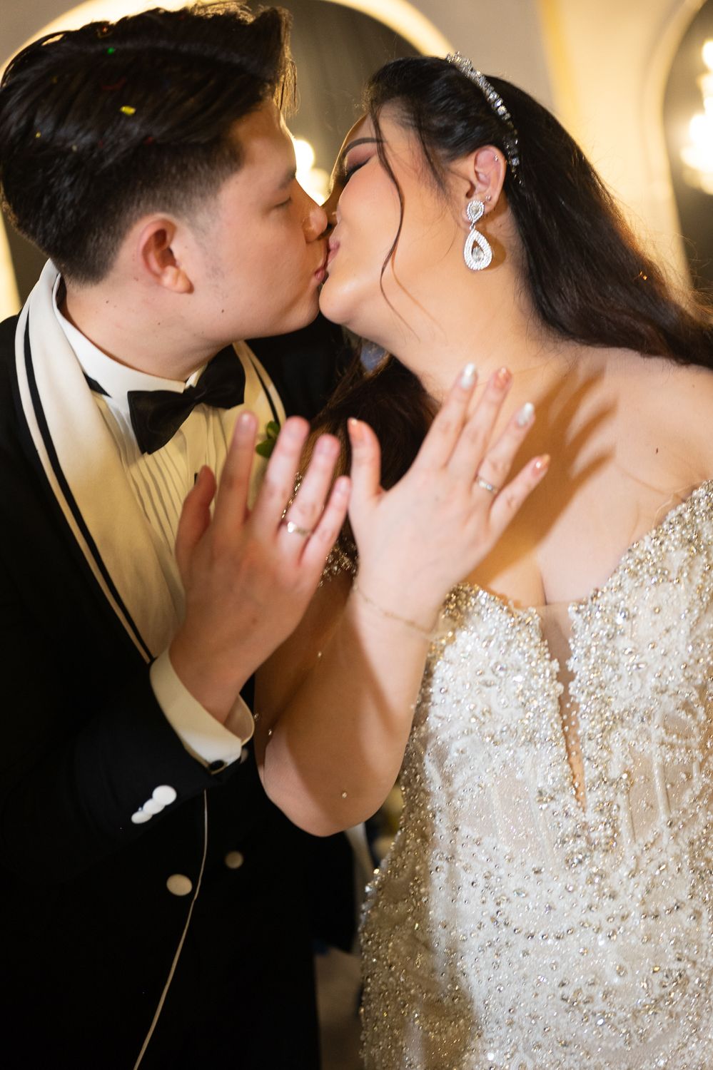 Bride and groom sharing a romantic kiss, wearing elegant wedding attire with sparkling jewelry and beaded gown.