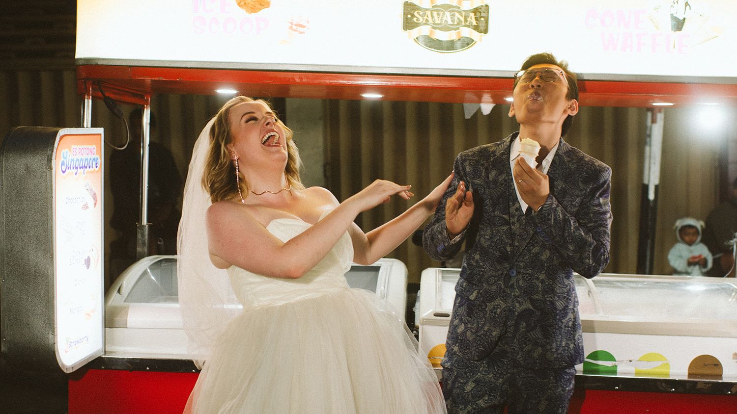 Bride and groom laughing joyfully at their wedding reception near a dessert cart.