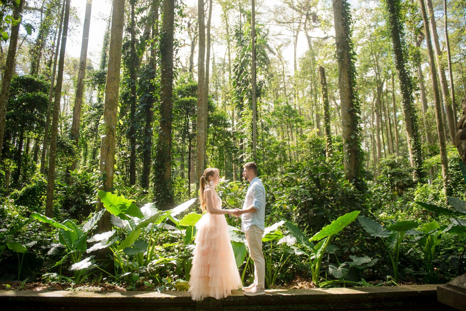 Couple holding hands in a lush tropical forest during a romantic outdoor wedding photoshoot.