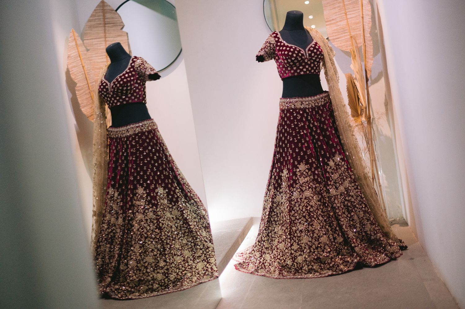 Elegant maroon bridal lehenga with gold embroidery displayed on mannequins in a boutique setting.