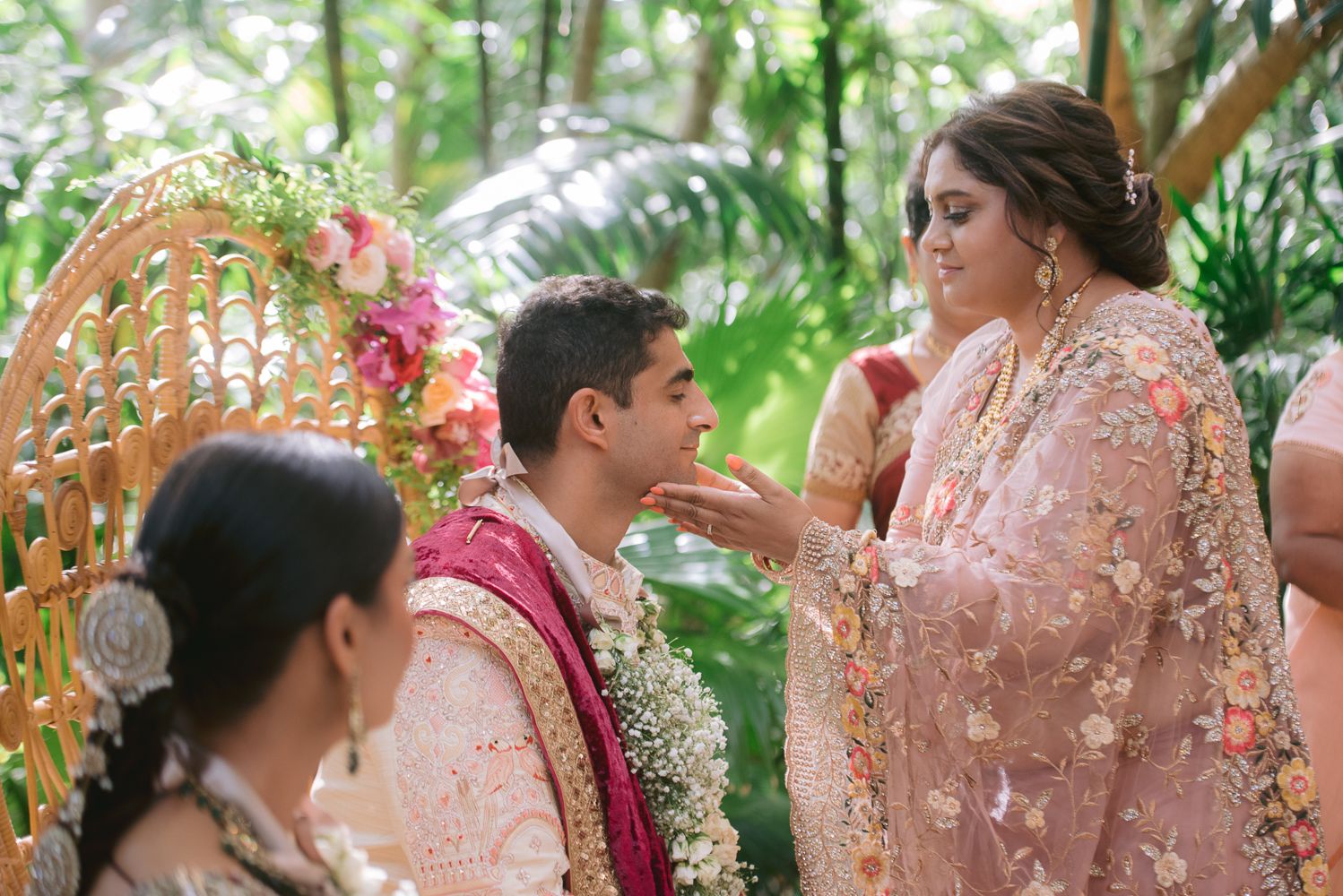 A bride in pink embroidered attire performs a wedding ritual with a groom in traditional Indian ceremony outdoors.