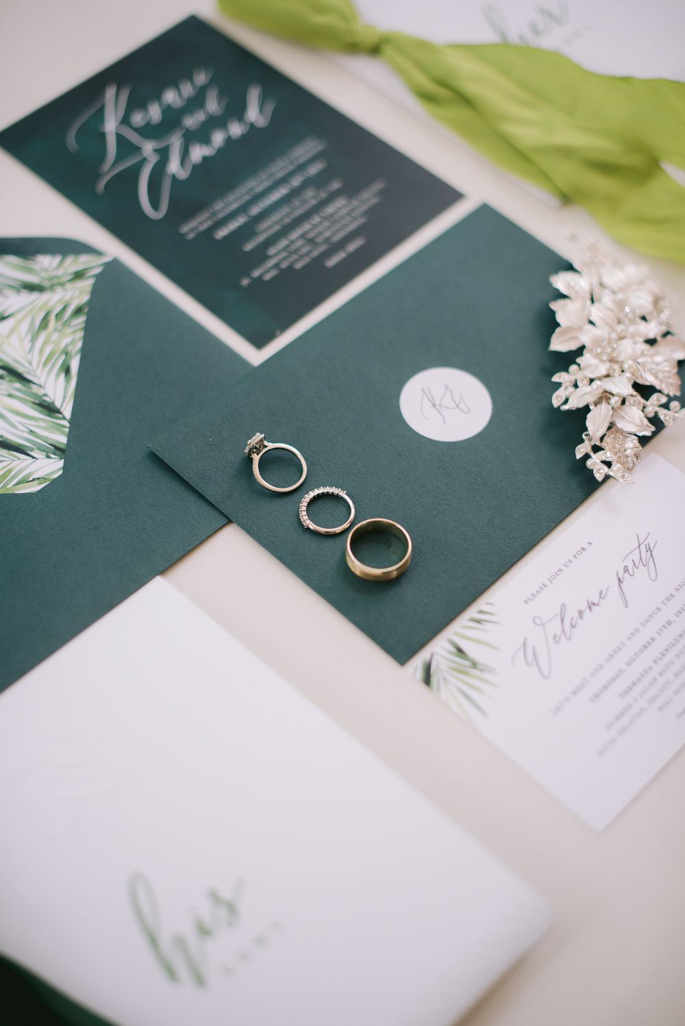 Elegant green wedding stationery suite with rings, tropical leaf details, and calligraphy invitations on white background.