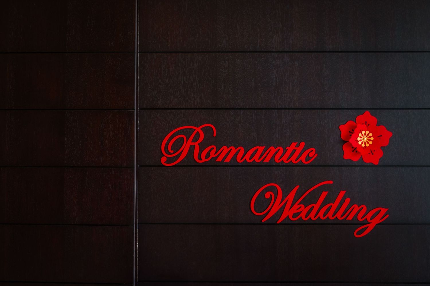 Red script text reading Romantic Wedding with a red flower emblem on a dark wood paneled wall.