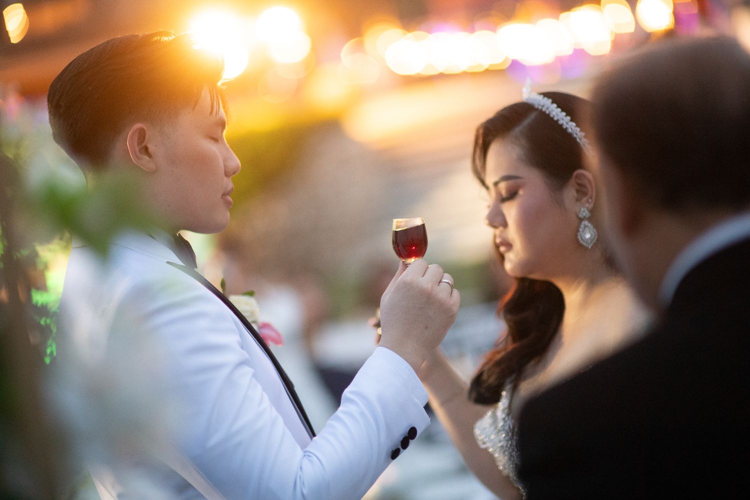 Bride and groom share a romantic wine toast at their elegant outdoor wedding reception at sunset.