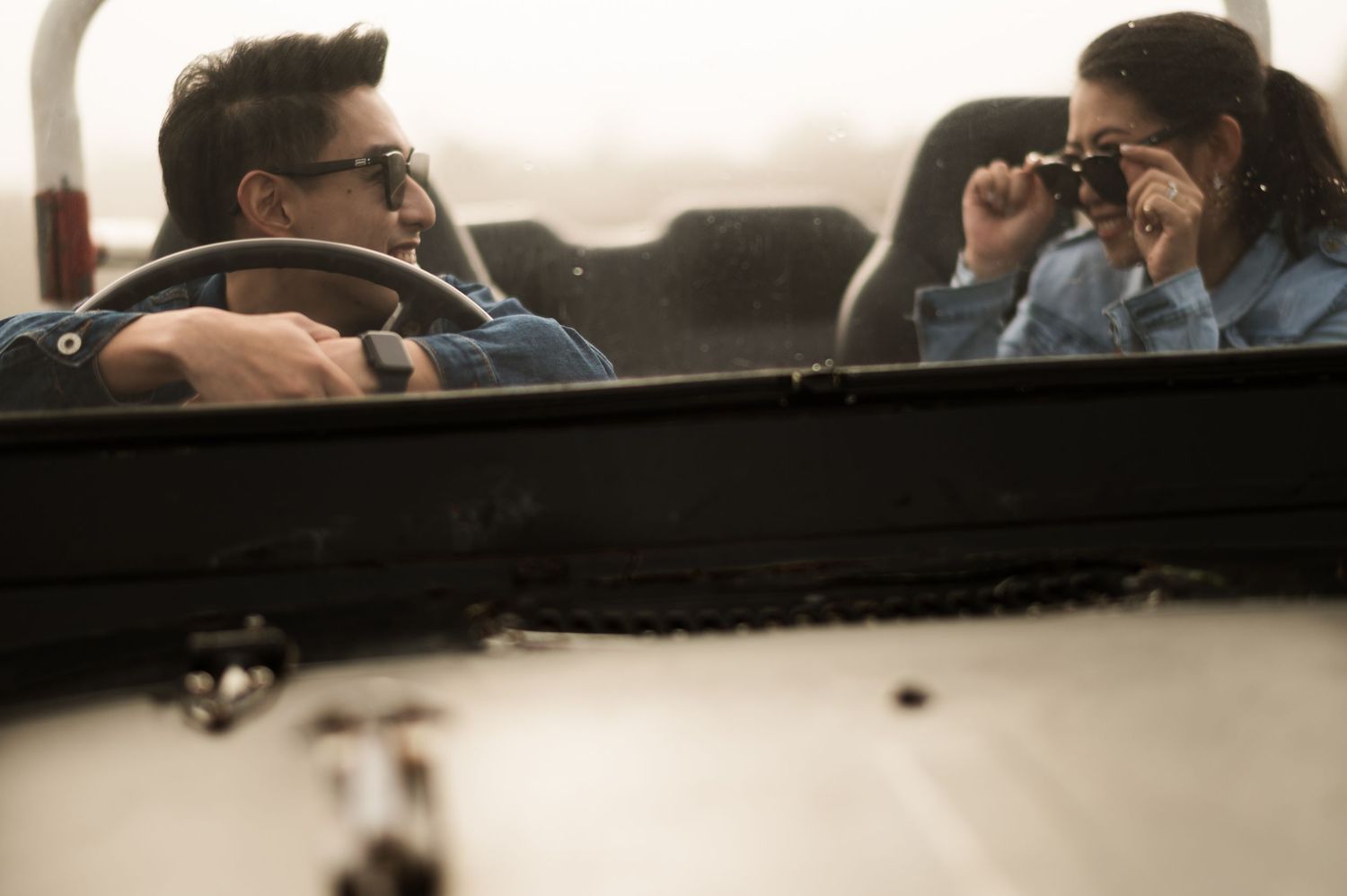A man driving a convertible car while a woman photographs with a vintage camera during a road trip.
