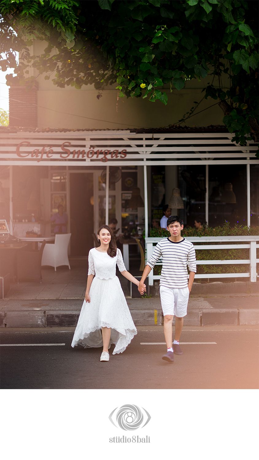 Couple holding hands walking in front of Cafe Smorgas, woman in white dress, man in striped shirt, outdoor setting.