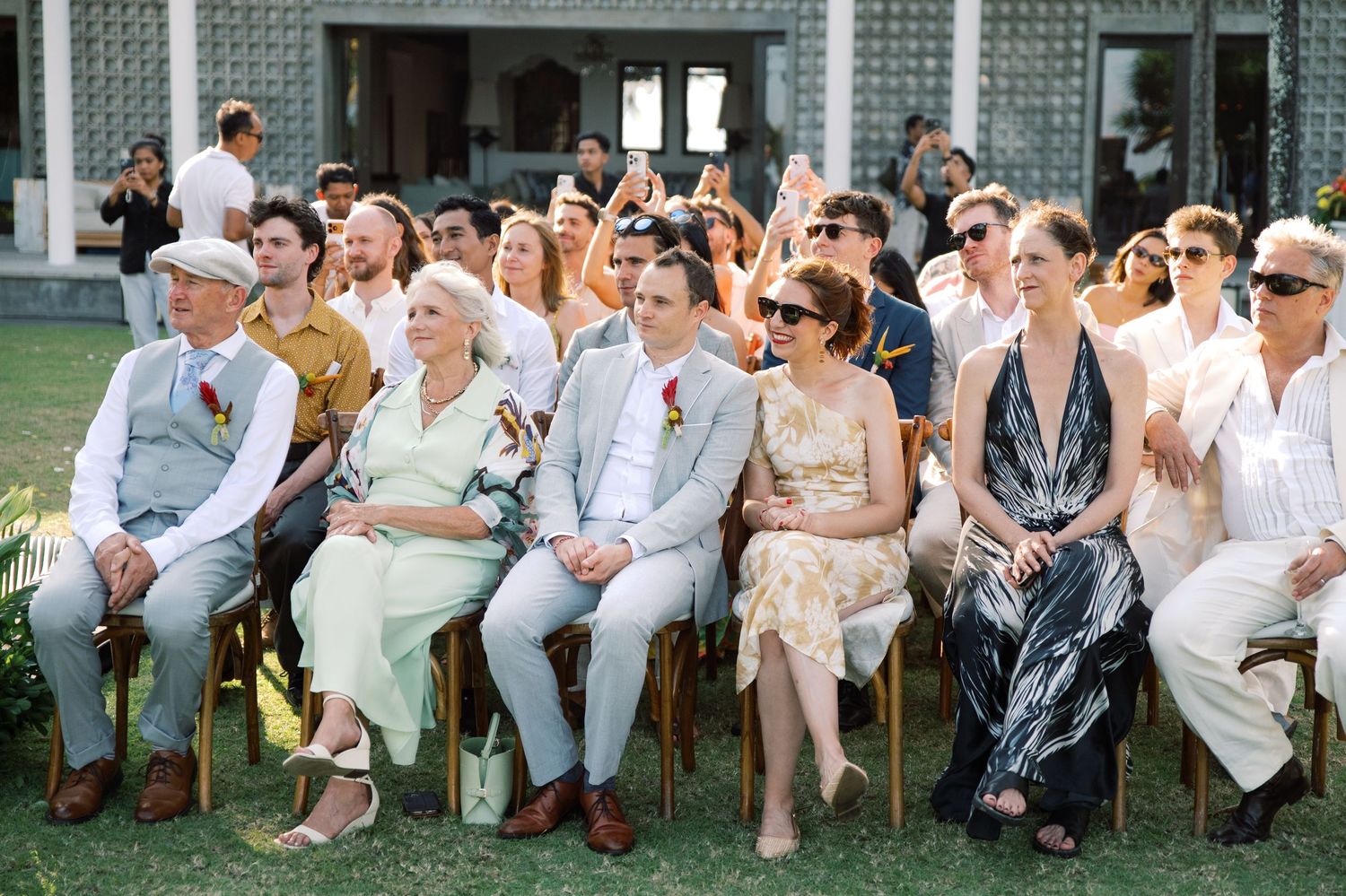 Wedding guests seated outdoors in casual attire enjoying a sunny garden ceremony celebration.