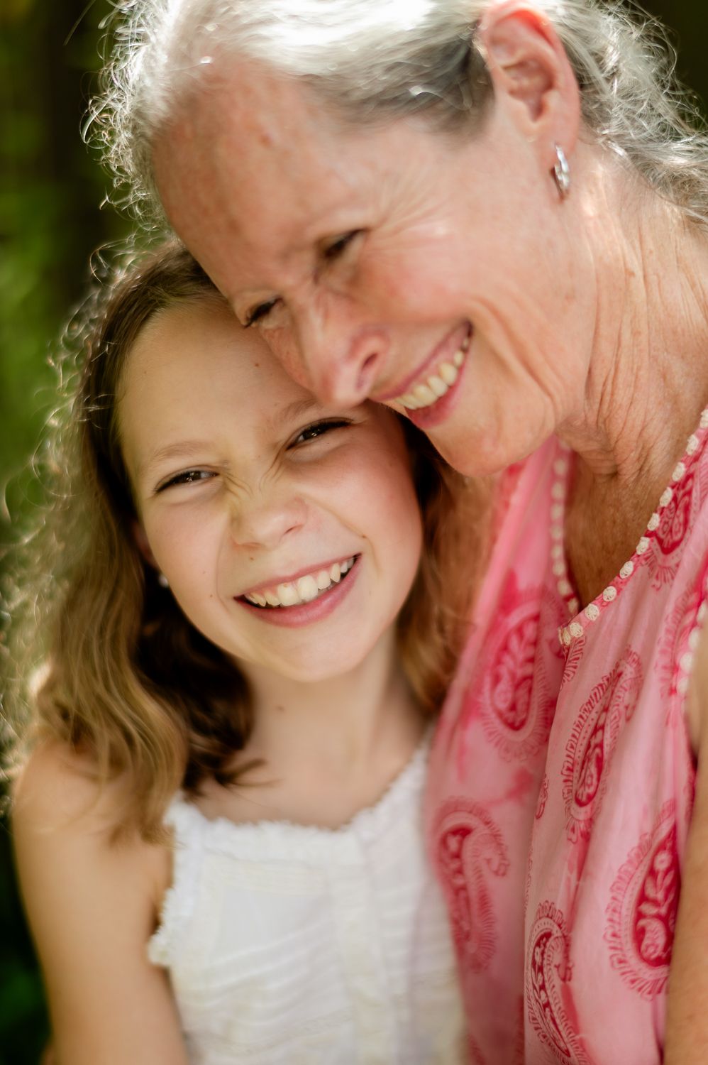 Smiling grandmother and granddaughter share a joyful embrace outdoors, both wearing pink and white.