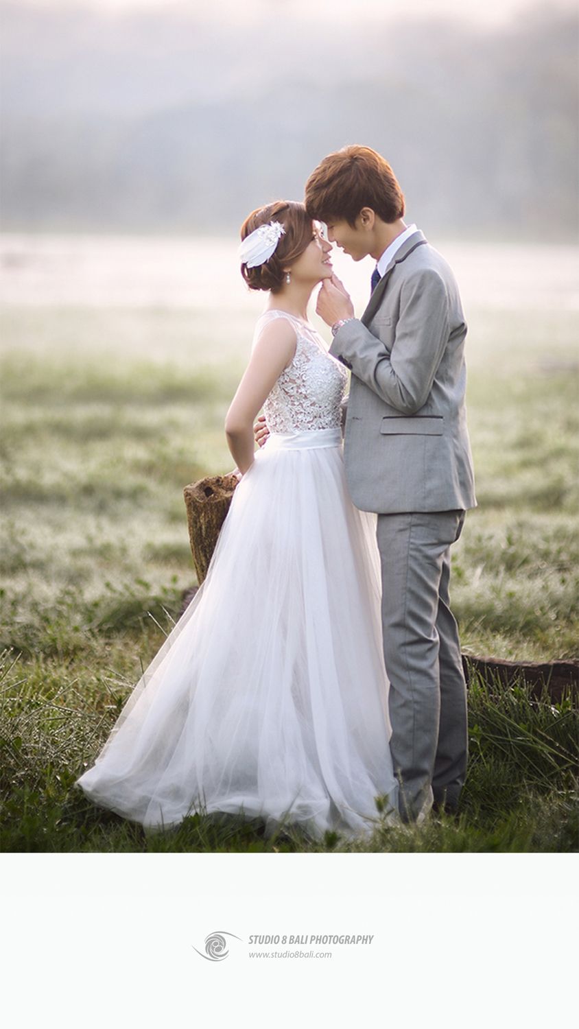 Romantic couple in wedding attire sharing an intimate moment in a misty field, bride in white gown, groom in gray suit.