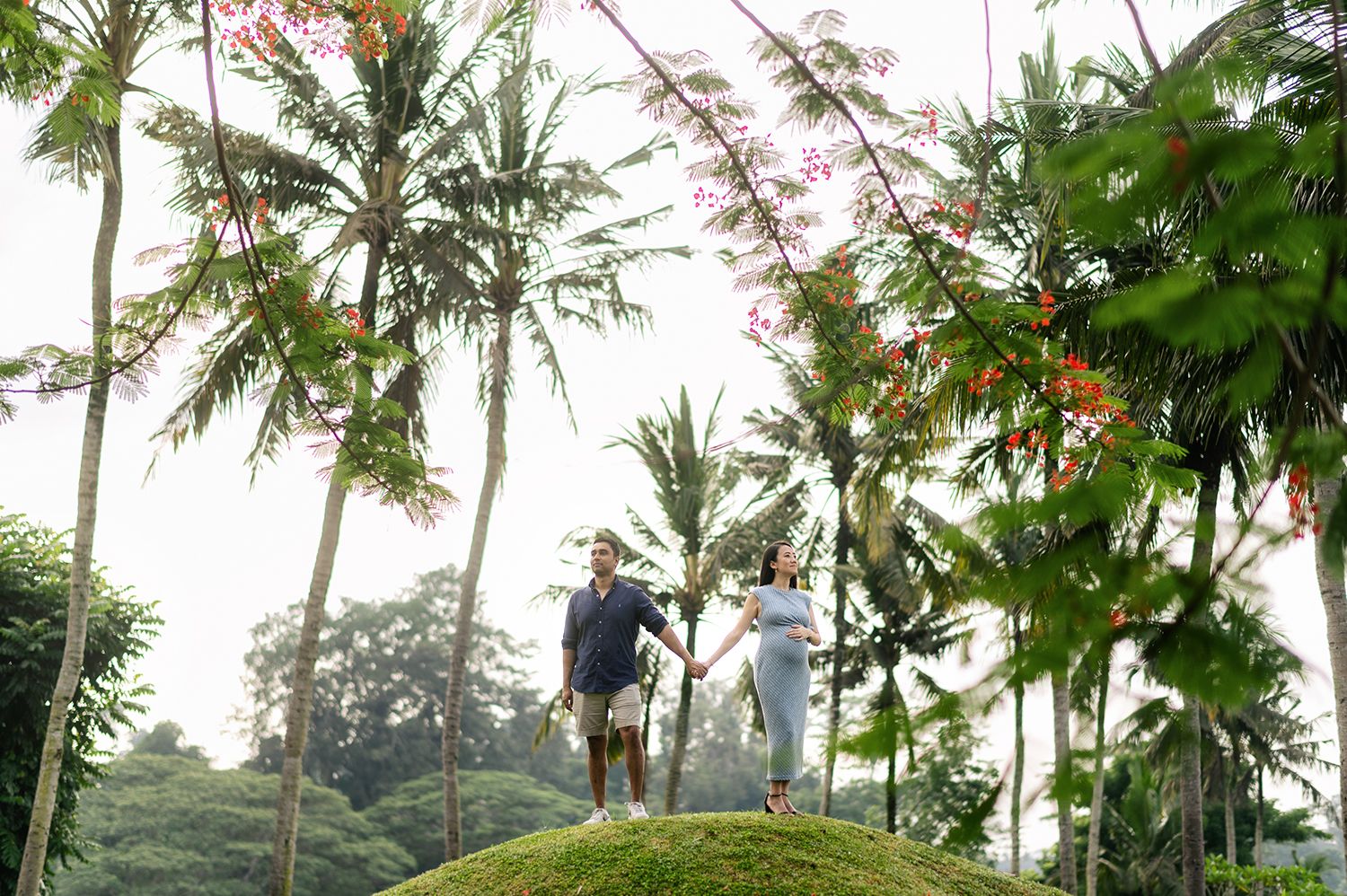 Couple standing on a moss-covered hill surrounded by tall palm trees in a lush tropical garden setting Maya Ubud Resort and Spa in Bali.