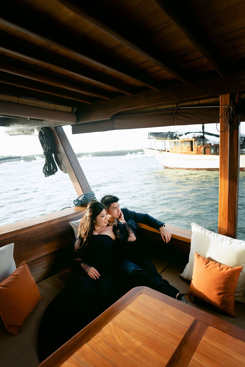 Couple cuddling on cushioned seating inside a wooden boat cabin on the water.