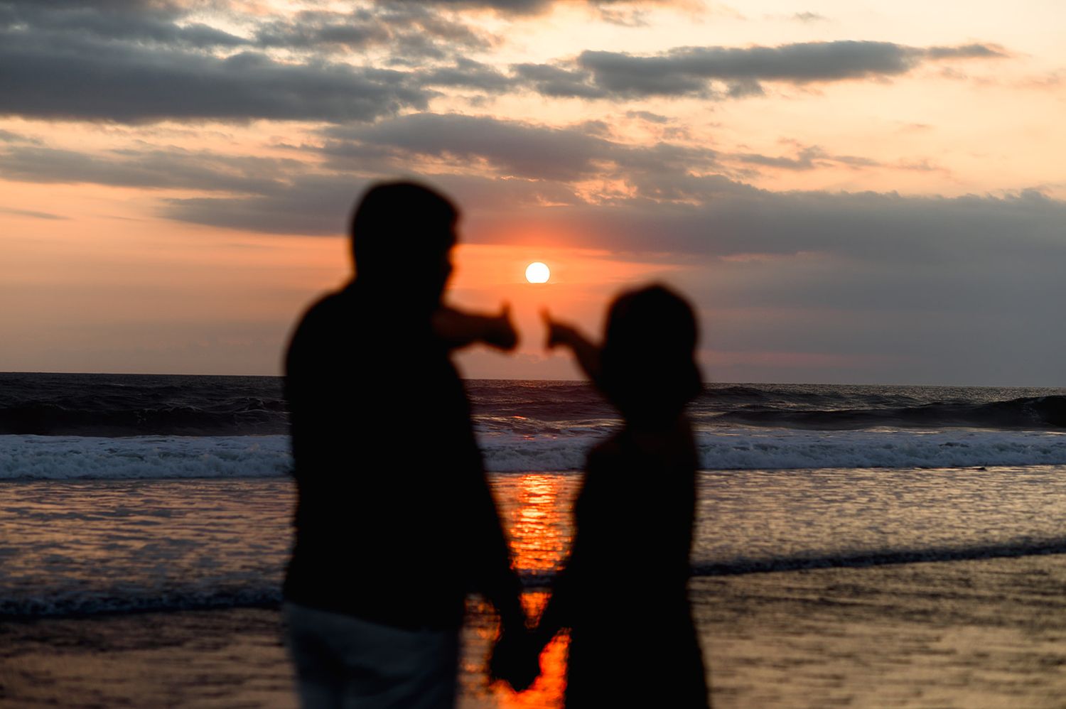 Silhouette of couple holding hands at sunset with ocean in the background.