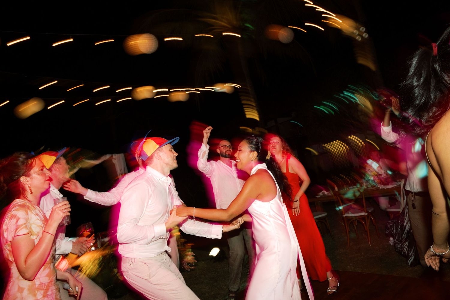Guests dancing energetically at a lively wedding reception party under colorful lights at night.