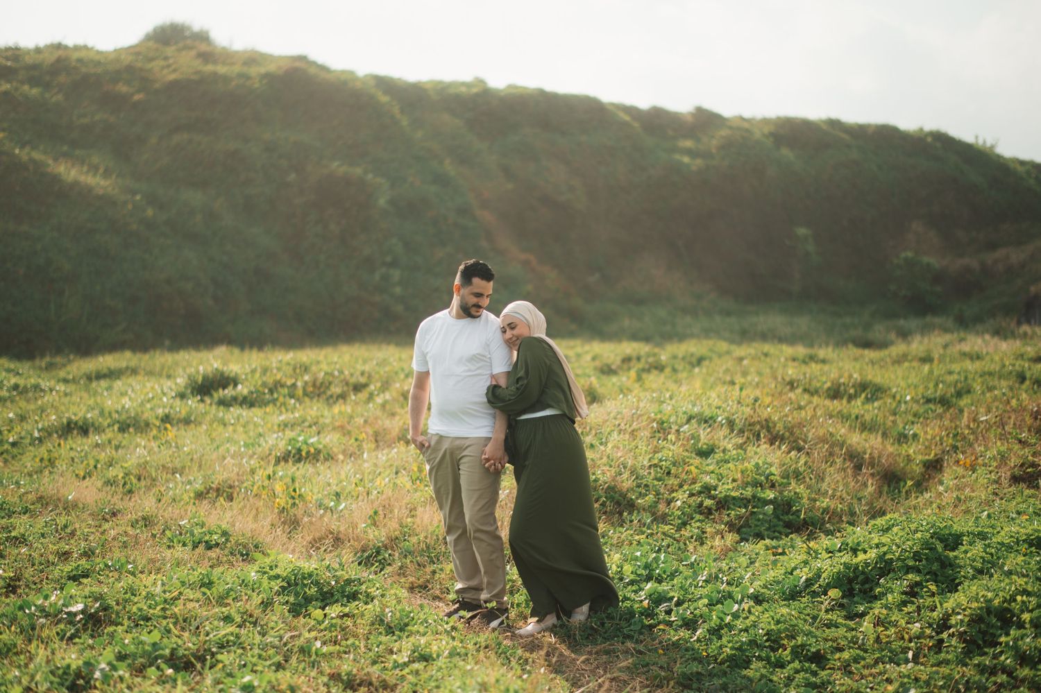 Two people walking together on a green hillside path in warm sunlight, one wearing a white shirt and the other a dark dress.
