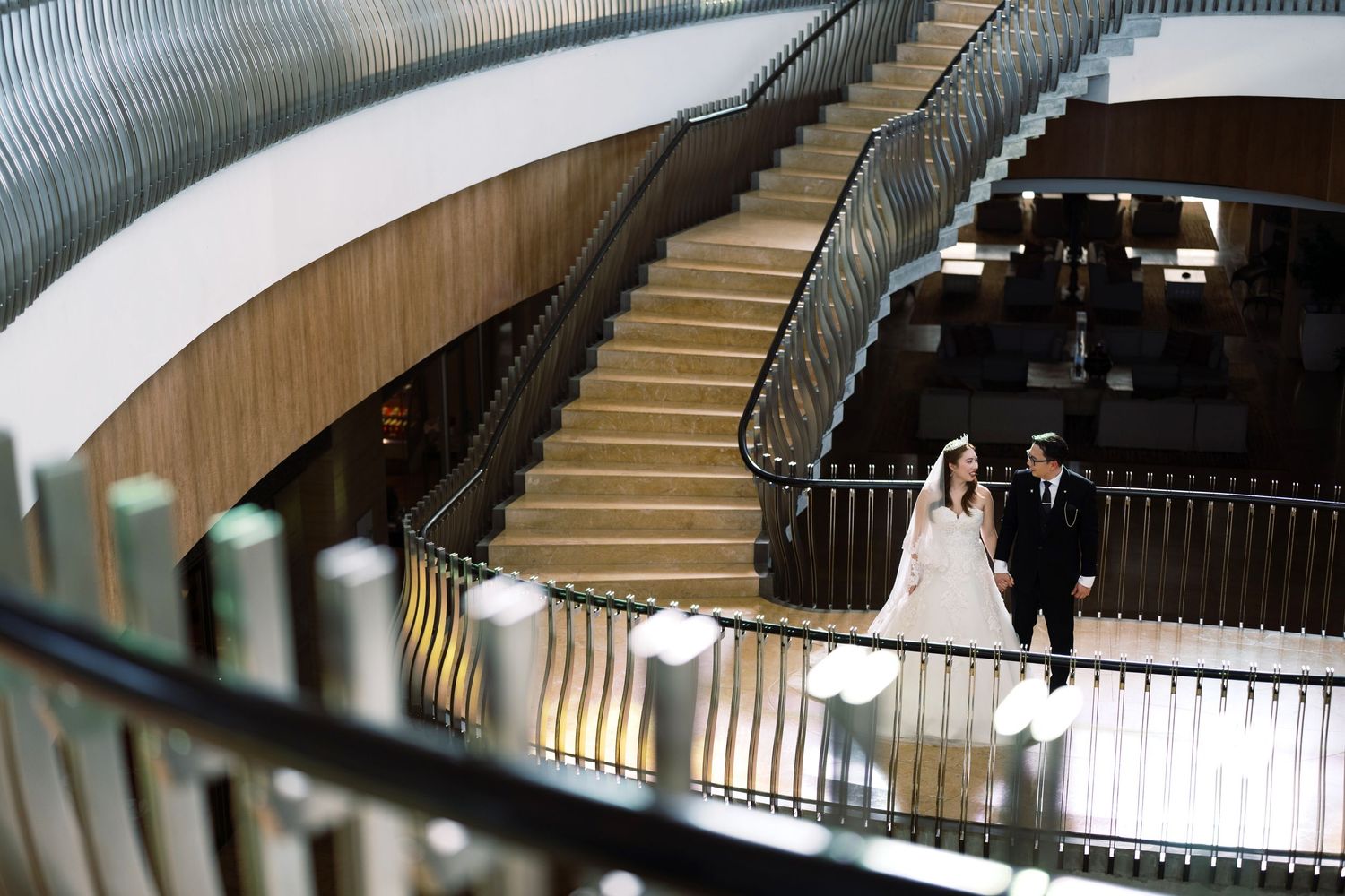 Bride and groom walking hand in hand on a grand staircase in an elegant modern venue.