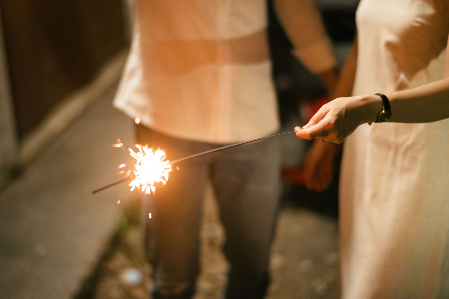 Person holding a lit sparkler at night during outdoor celebration event.