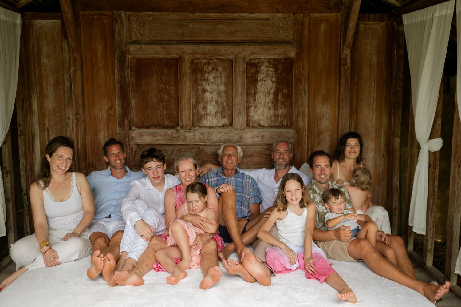 Large multigenerational family posing together on a white bed in a rustic wooden room.