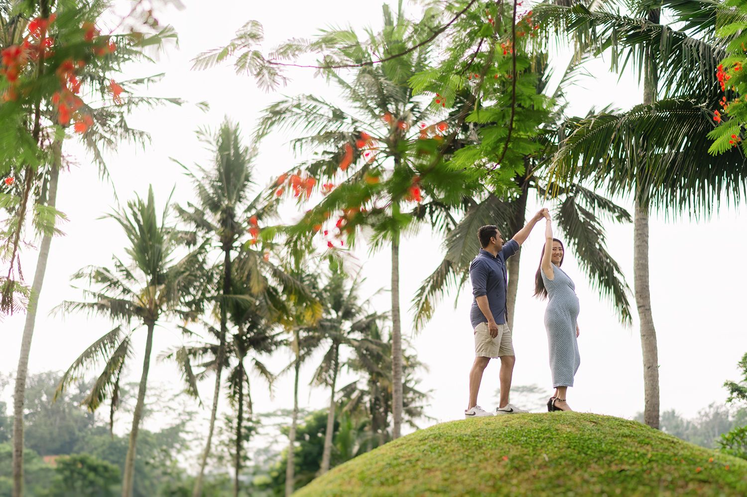 Couple holding hands on a lush green hill surrounded by tall palm trees in a tropical Bali setting Maya Ubud Resort and Spa in Bali.