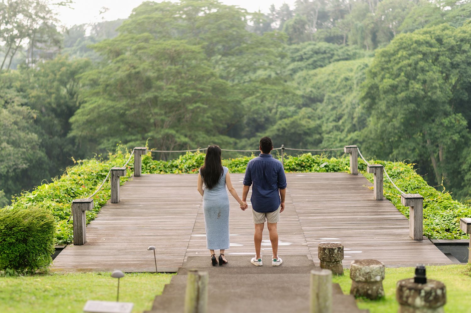 Couple holding hands on a wooden deck surrounded by lush green tropical gardens and trees Maya Ubud Resort and Spa in Bali.