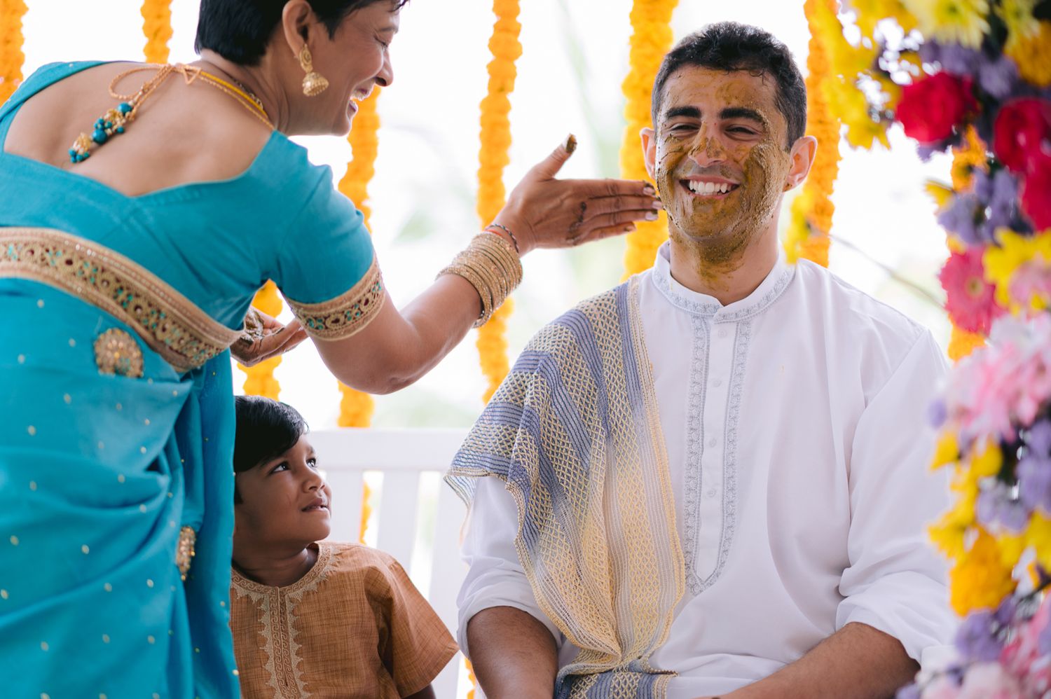 Woman applying turmeric paste on groom's face during traditional Indian Haldi wedding ceremony.
