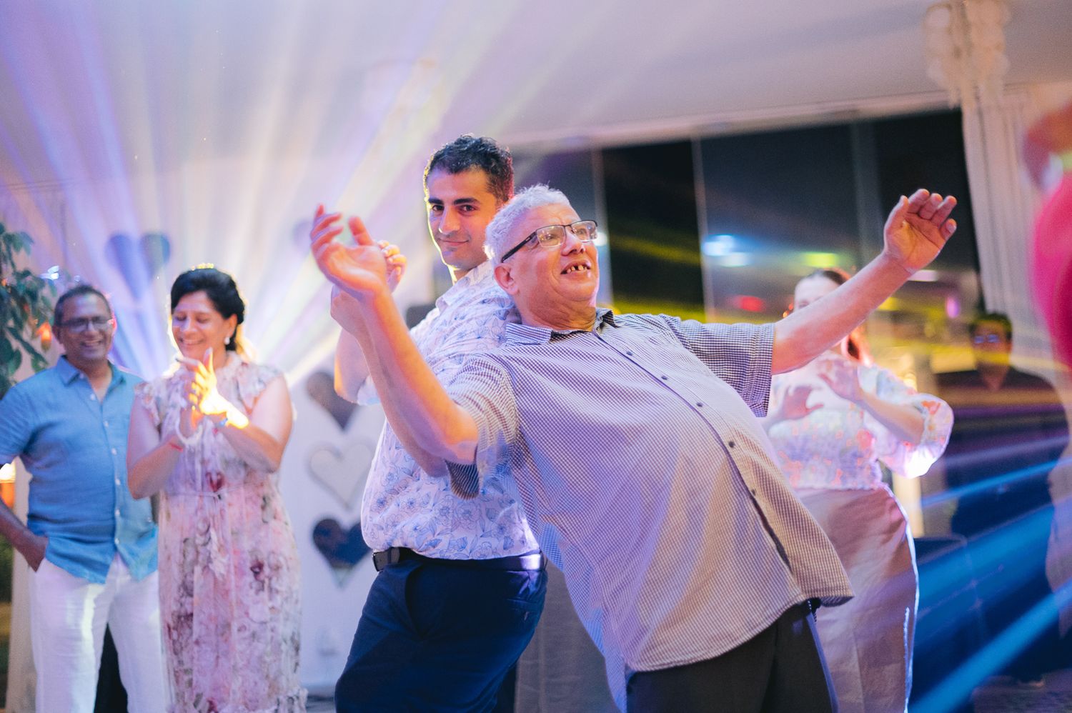 People dancing joyfully at an indoor celebration event with colorful lights in the background.