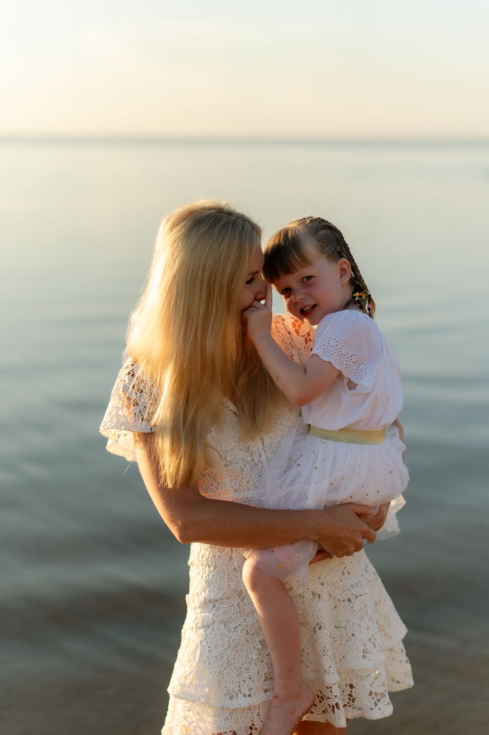 Loving mother holding her young daughter close on a calm beach during golden hour sunset.