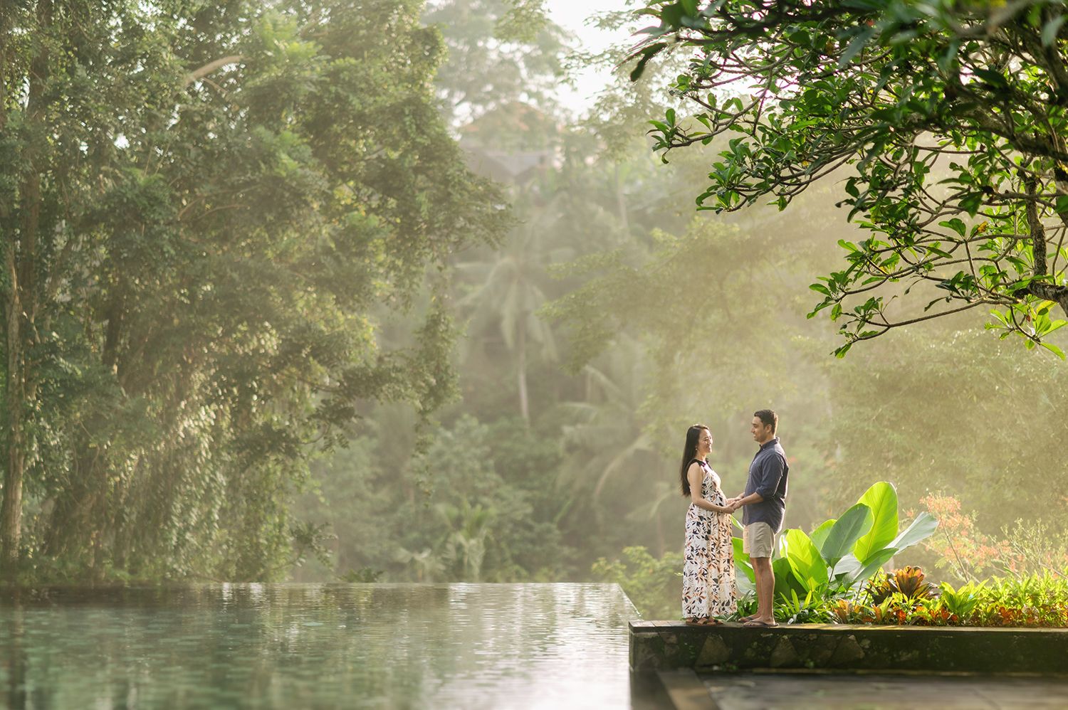 Couple standing by a misty infinity pool surrounded by lush tropical greenery in a romantic outdoor setting Maya Ubud Resort and Spa in Bal.