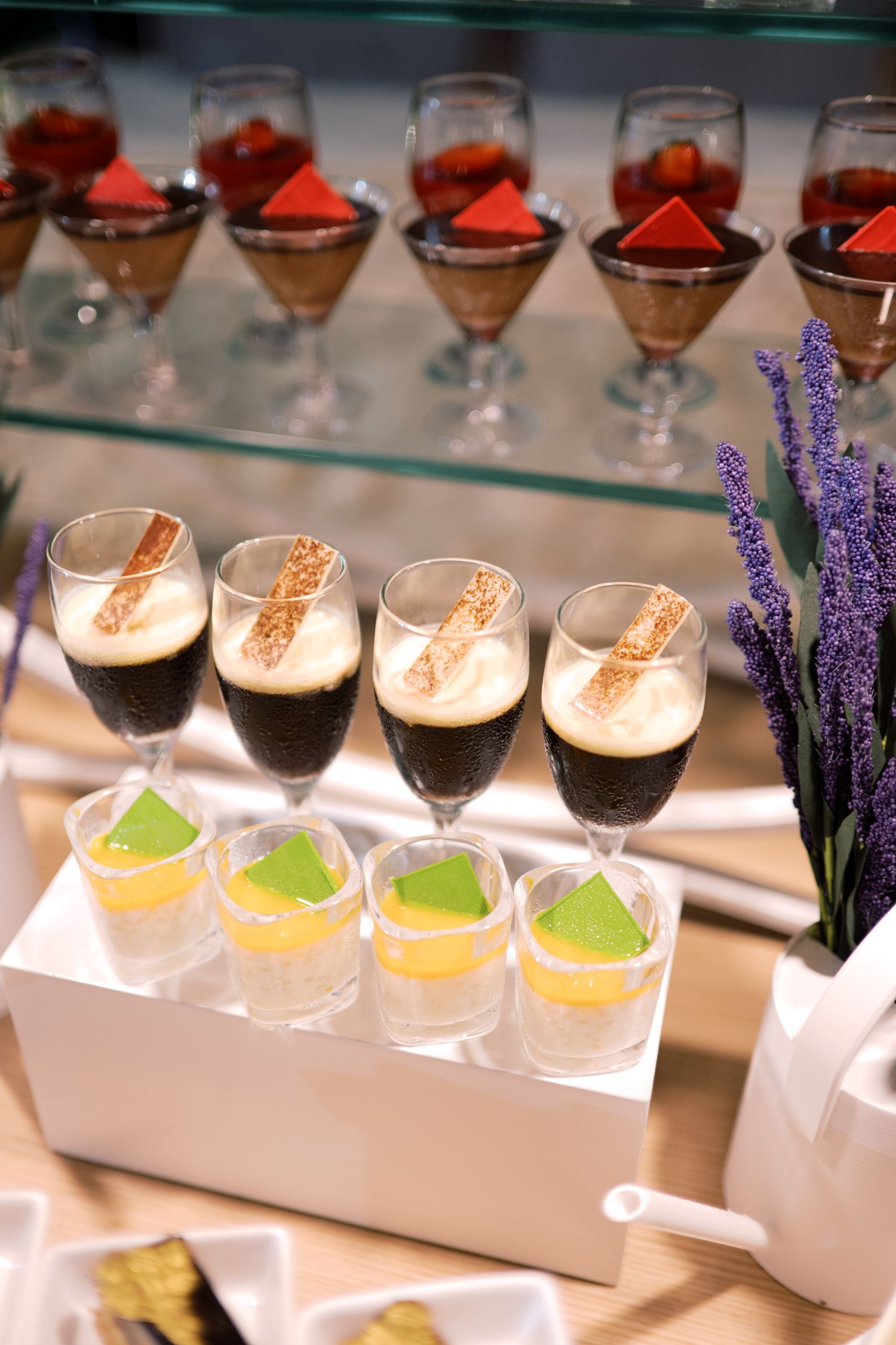 Elegant dessert display with layered chocolate mousse glasses, colorful gelatin shots, and lavender decor on a buffet table.