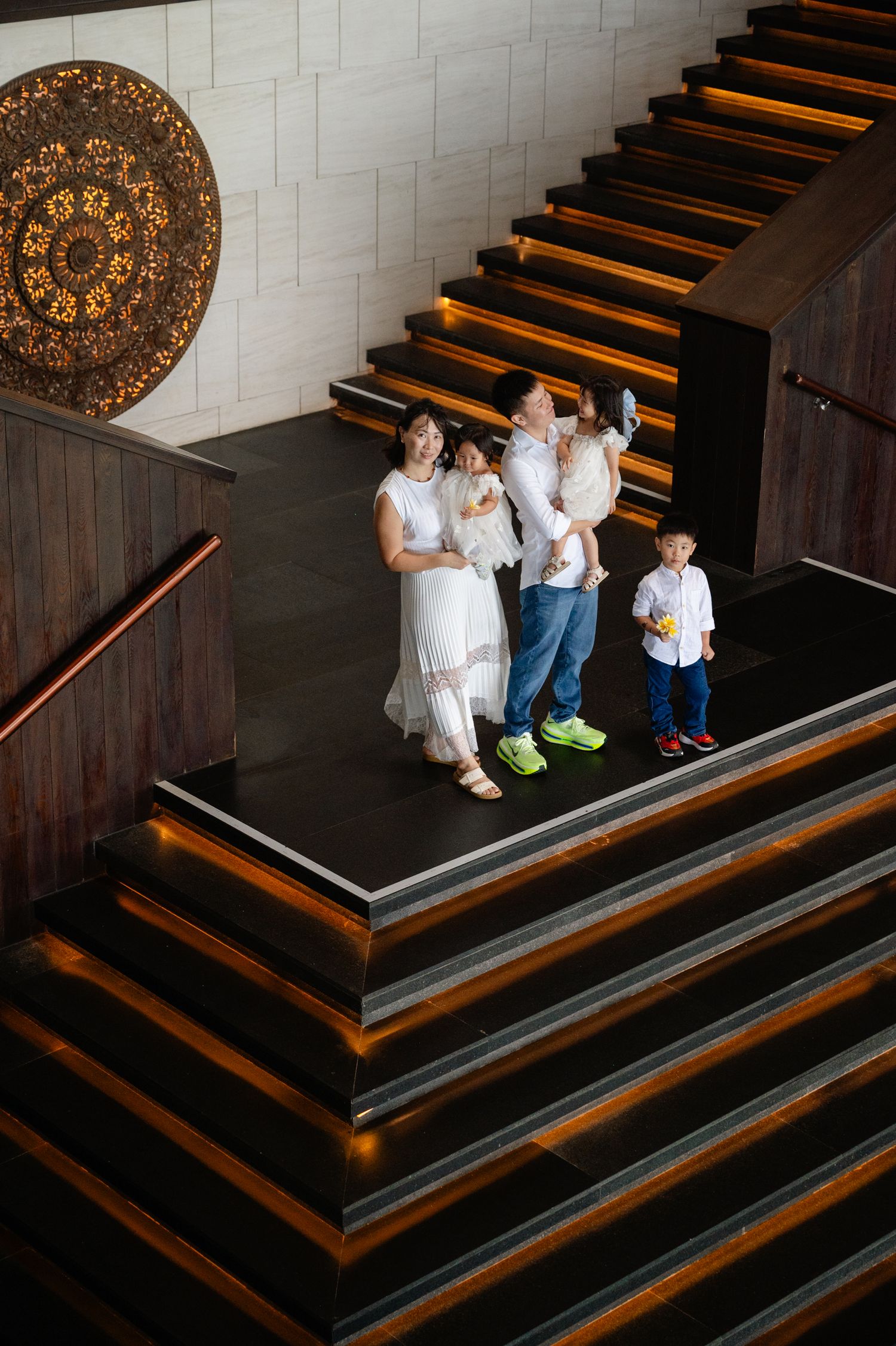 Family posing together on grand staircase landing with ornate decor, viewed from above in elegant interior.