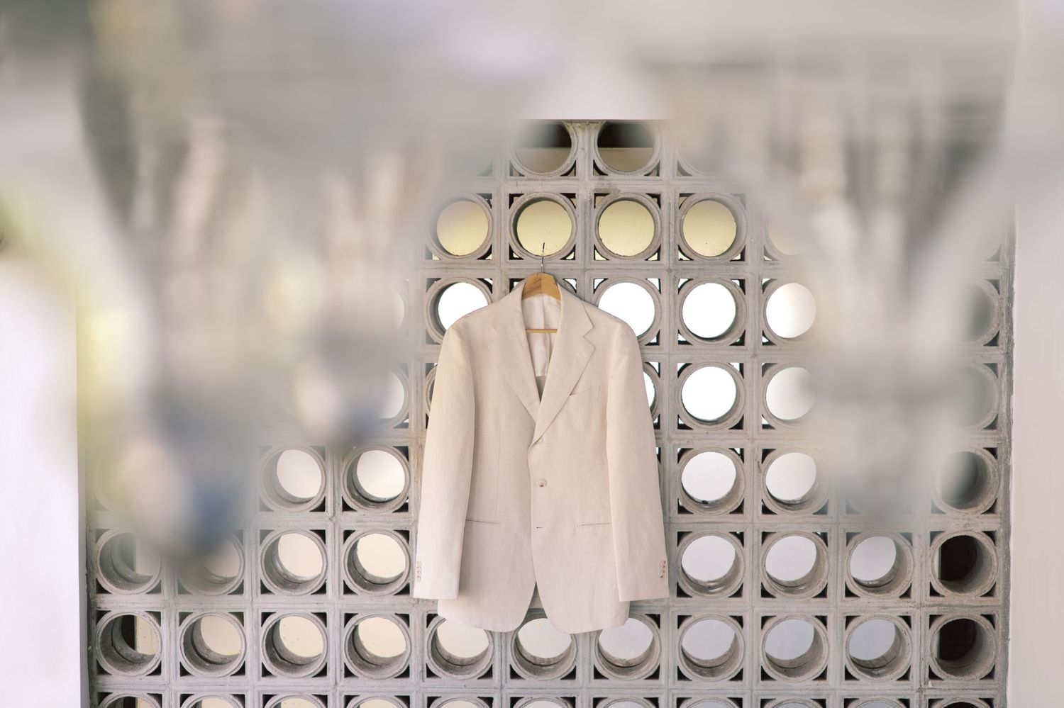 A white blazer jacket hanging on a decorative lattice wall with circular cutouts in a bright retail store.
