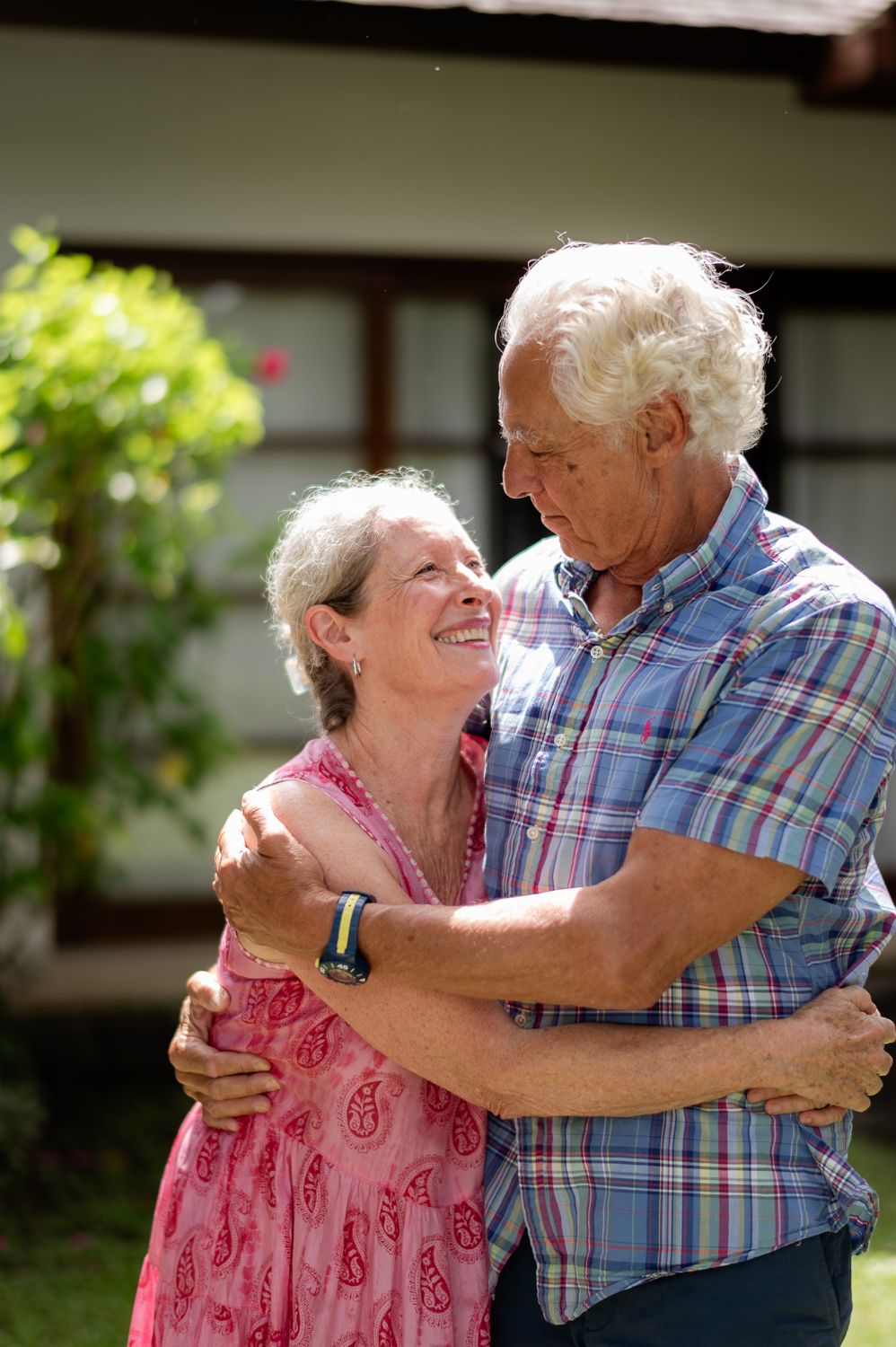 Happy senior couple dancing together in sunny garden, sharing a joyful embrace outside their home.