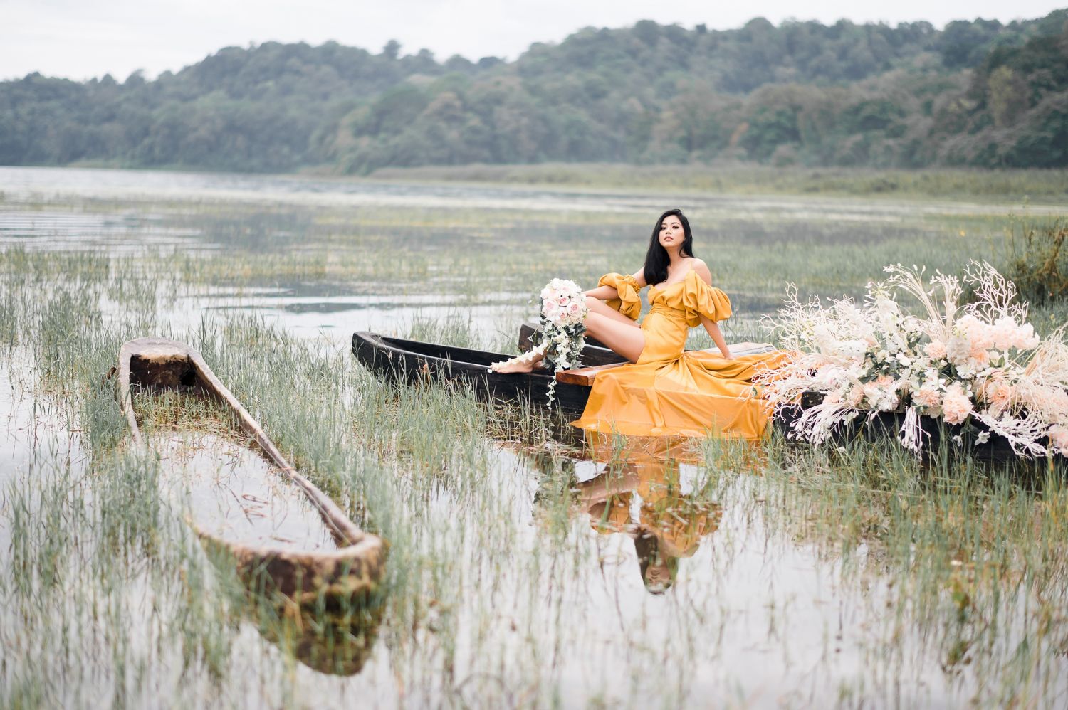 Woman in yellow dress sitting in rustic boat surrounded by florals on a serene lake.